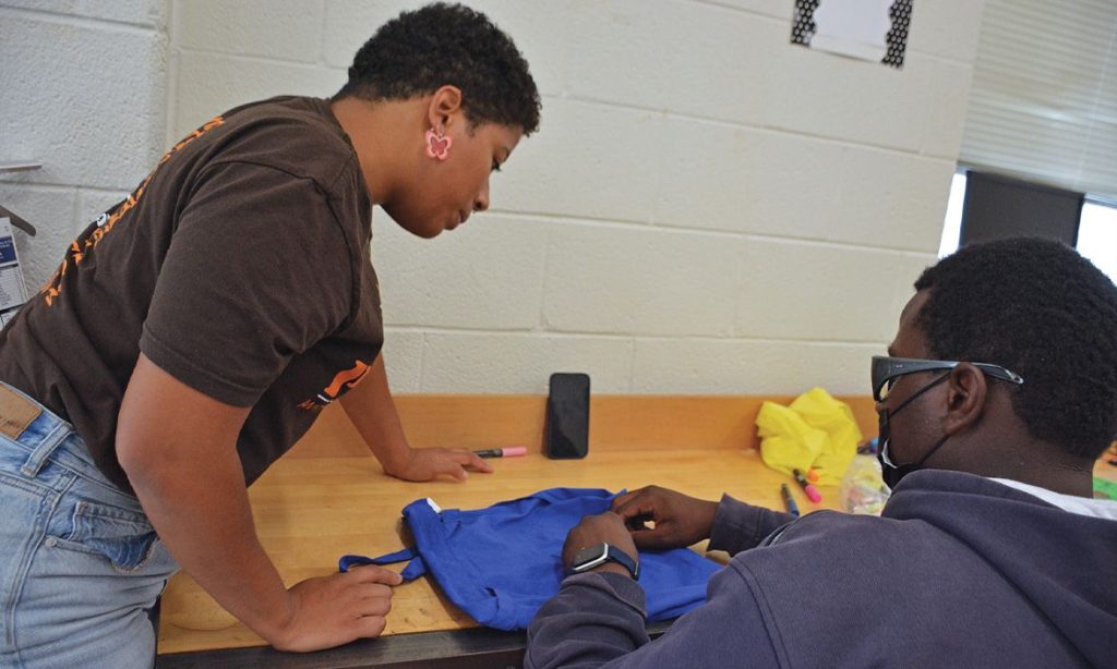 Duke student Ezra Belgrave, left, helps Durham high school students refine the circuitry of their high-tech handbags as part of the “Inspiring the Next Generation of STEM Learners” research project. Photo by Stephen Schramm.